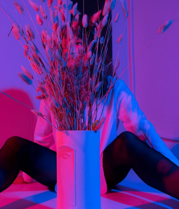 Woman in a graceful yoga pose against a dark background with pink light.